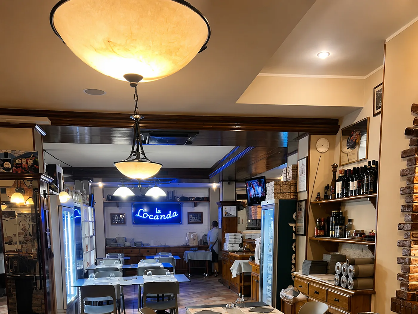 La sala interna della Locanda, tavoli apparecchiati e insegna luminosa